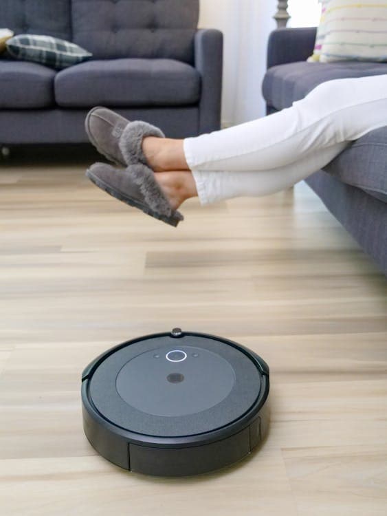 Robot vacuum cleaner on floor with person relaxing on sofa