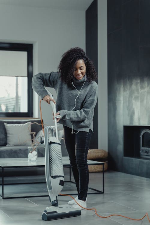 Woman vacuuming living room floor with cordless upright vacuum cleaner