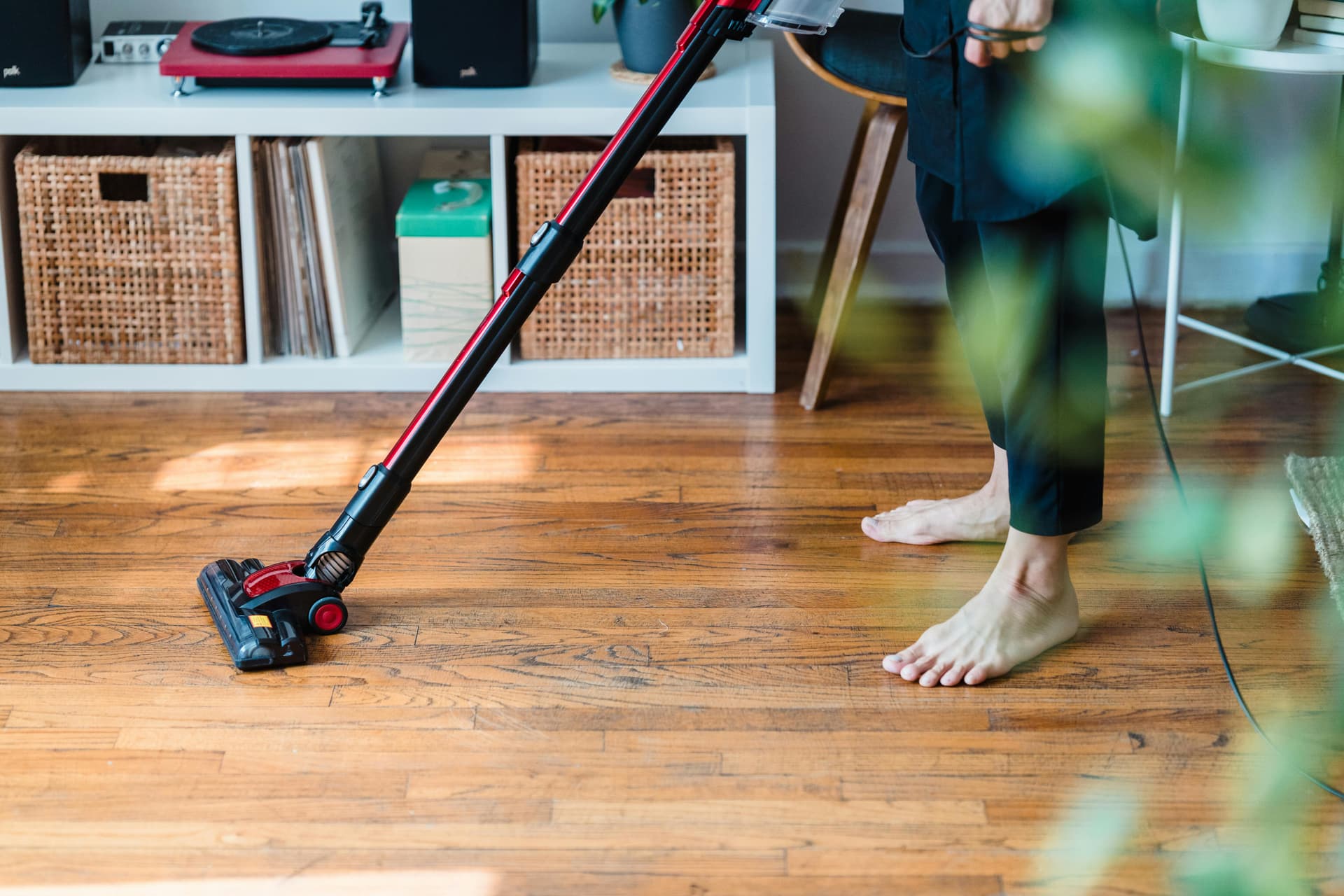 Woman vacuuming living room floor with cordless upright vacuum cleaner